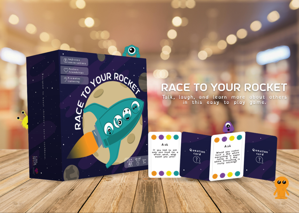 Race To Your Rocket game box with 4 playing cards fanned out in front. Set up on a wooden table.